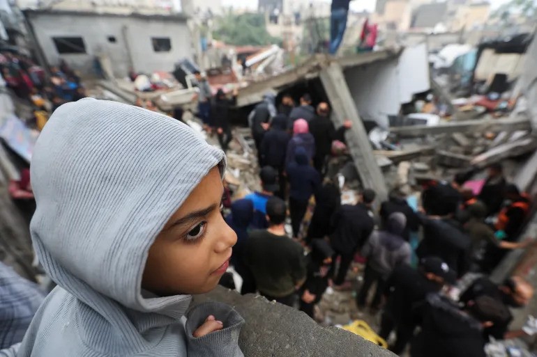 A child looks on as Palestinians inspect the damage at the site of Israeli air strikes on houses in Khan Younis in the southern Gaza Strip, on December 13, 2023 [Abu Mustafa/Reuters]