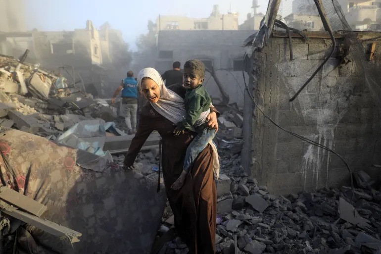 A woman flees with her child as Israeli airstrikes devastate the Maghazi refugee camp in central Gaza [Yasser Qudih/AFP]